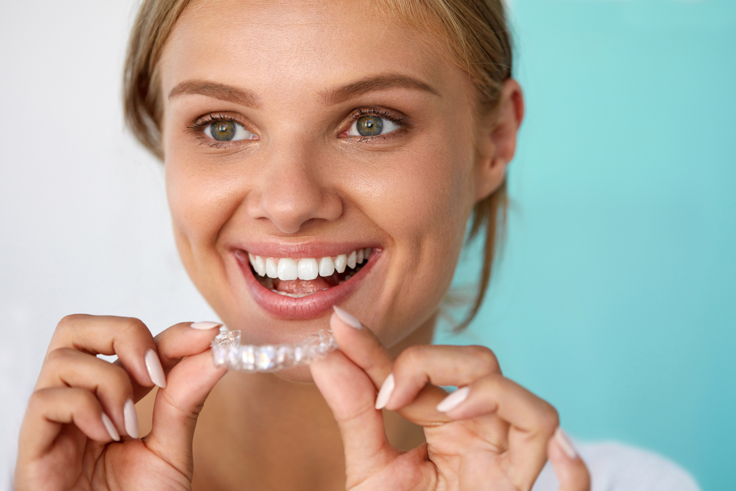 Lady smiling whilst holding her clear Invisalign aligners