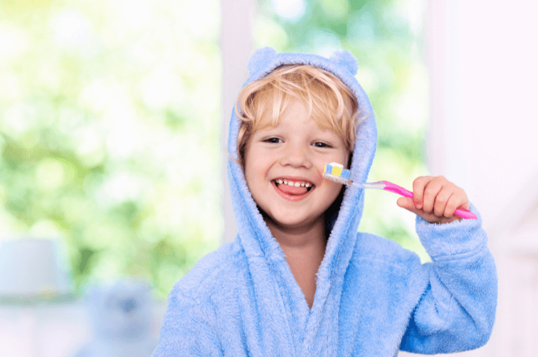 Image of young child cleaning his teeth in blue dressing gown with bunny ears.